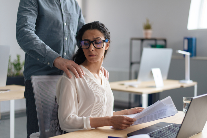 male employee touching disgusted woman in an office